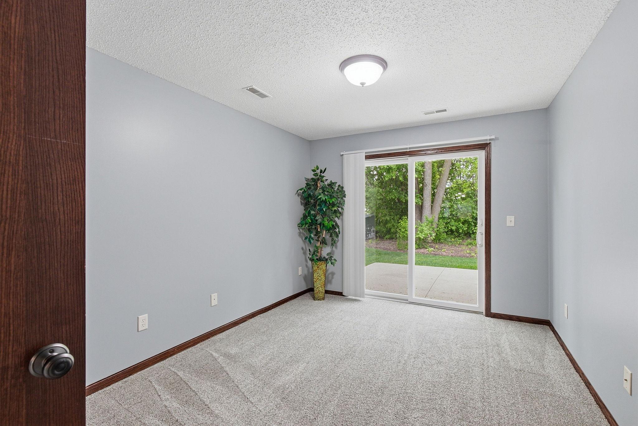 Cozy carpeted room with sliding glass doors leading to a private patio and peaceful, tree-lined backyard.