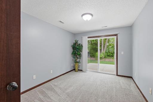 Cozy carpeted room with sliding glass doors leading to a private patio and peaceful, tree-lined backyard.