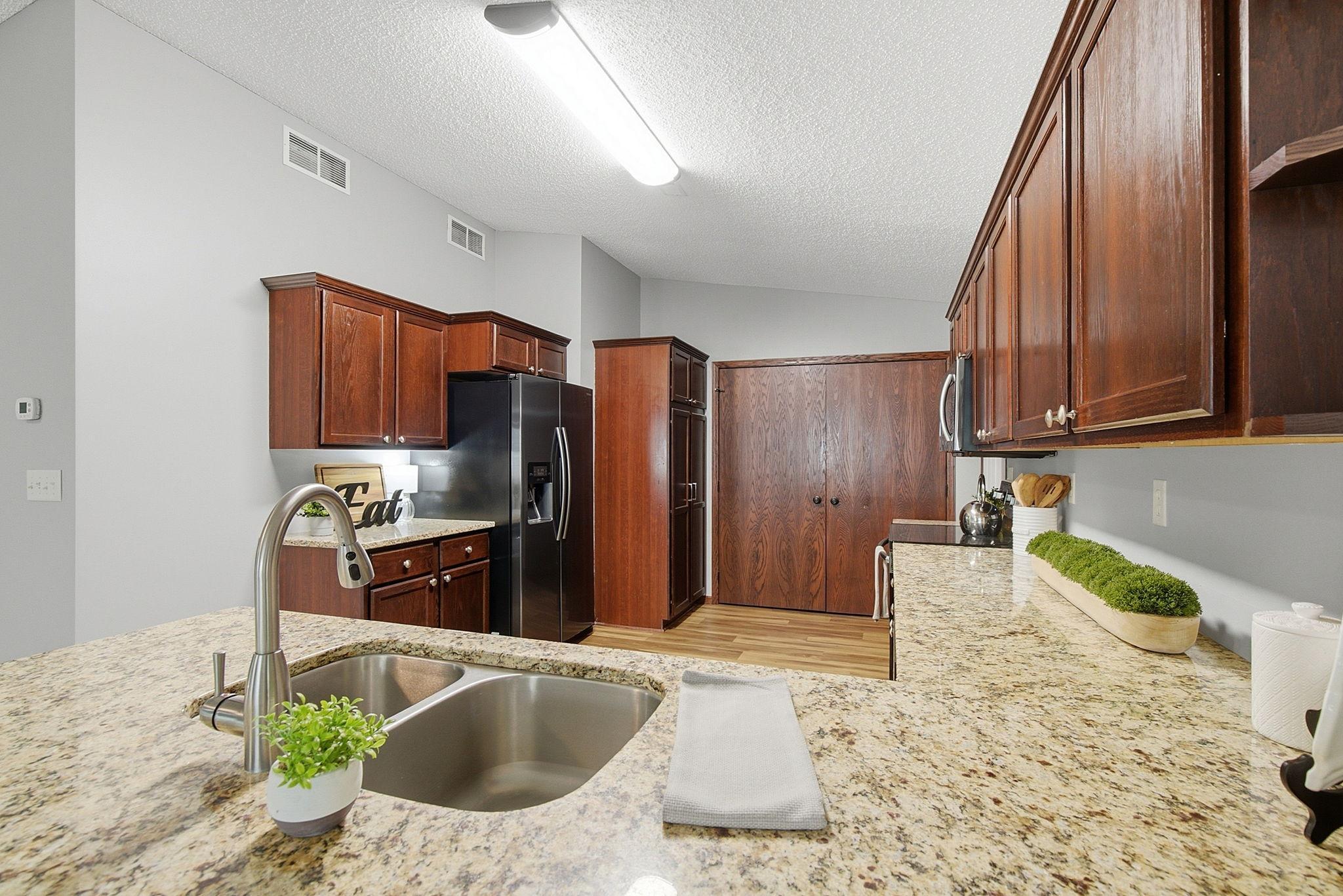 Spacious kitchen with granite countertops, double-basin undermount sink, black appliances, and rich wood cabinetry offering ample storage.