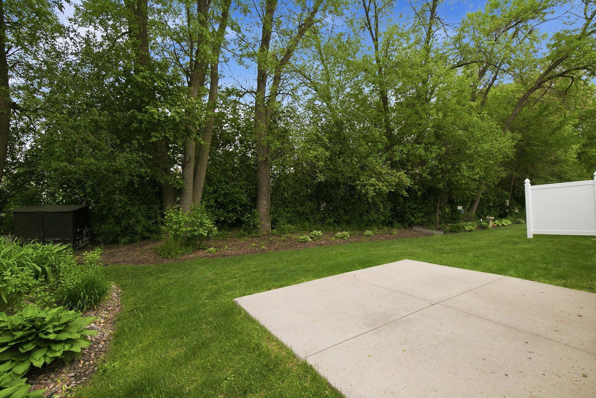 Peaceful backyard retreat with a concrete patio, lush green lawn, and mature trees providing natural privacy.
