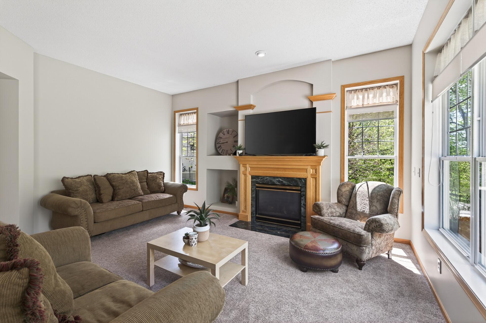 Warm and welcoming living space with abundant natural light, fireplace focal point, and peaceful treetop views.