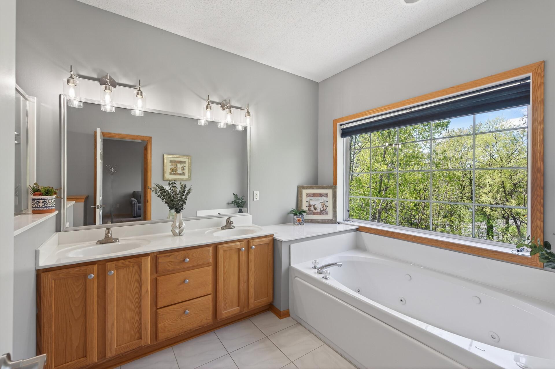 Spacious owner’s bathroom with double vanity, soaking tub, and serene treetop views.