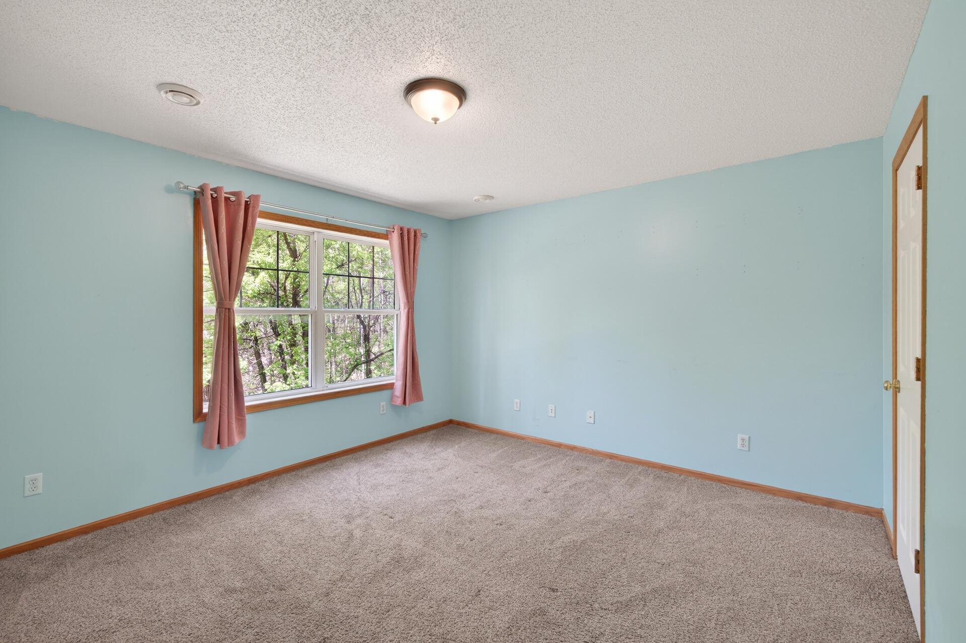 Bright secondary bedroom on lower level with large window, soft natural light, and ample floor space.