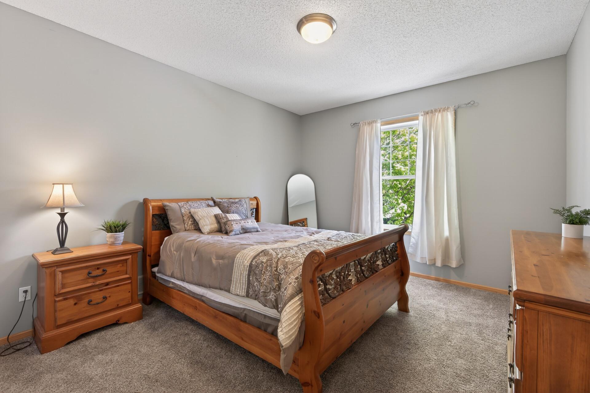 Inviting guest bedroom with warm wood furnishings, neutral tones, and abundant natural light.