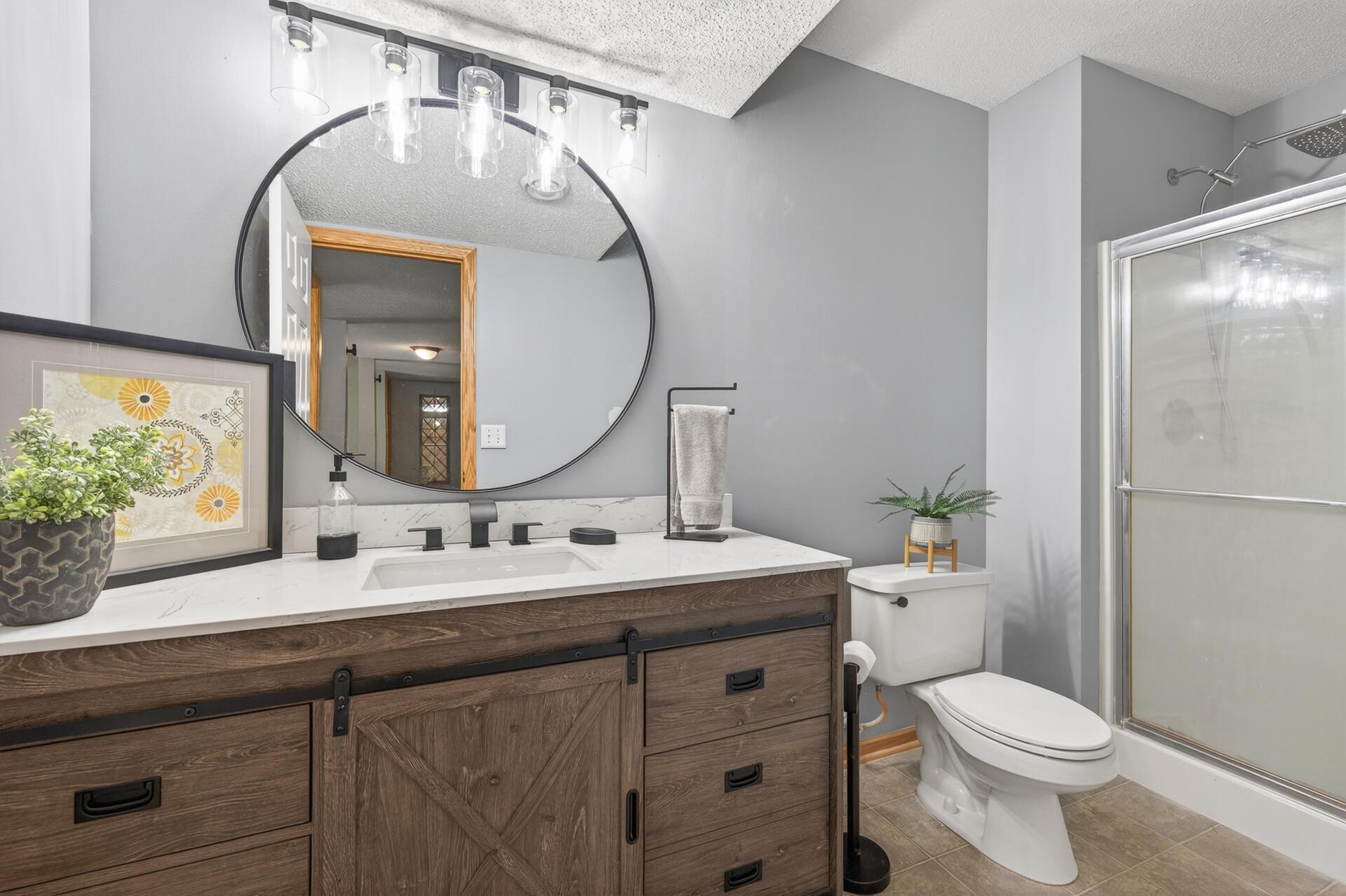 Beautifully updated lower-level bathroom featuring custom vanity, quartz-style countertop, modern fixtures, and walk-in shower.