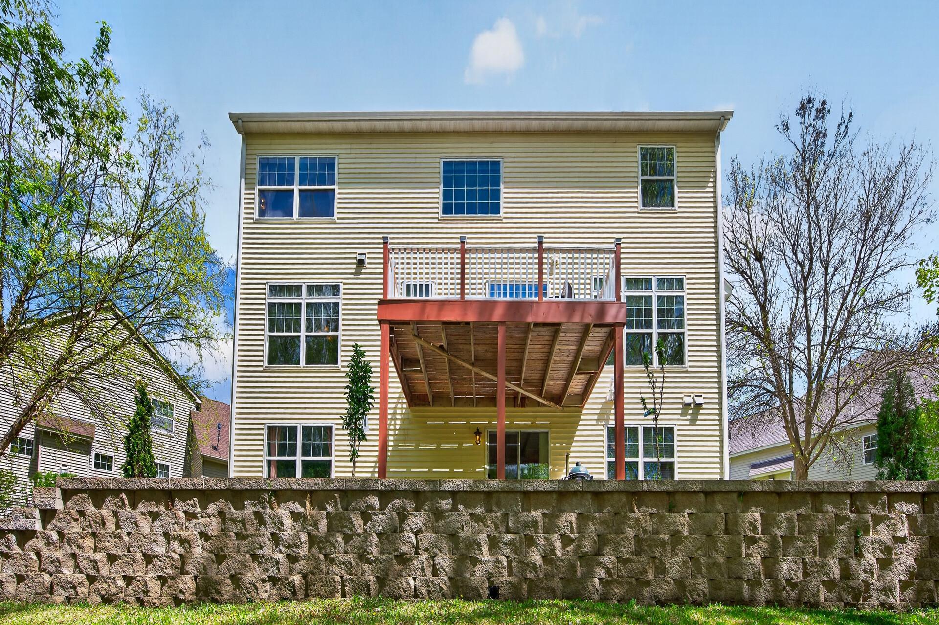 Rear exterior showcasing multi-level outdoor living spaces, walkout lower level, and retaining wall landscaping.