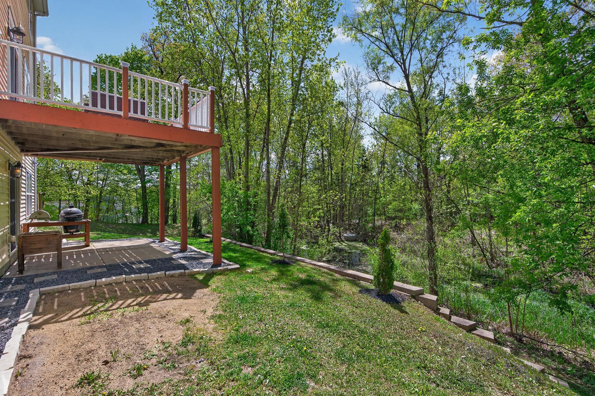 Expansive backyard with elevated deck, lower patio space, and scenic wooded backdrop.