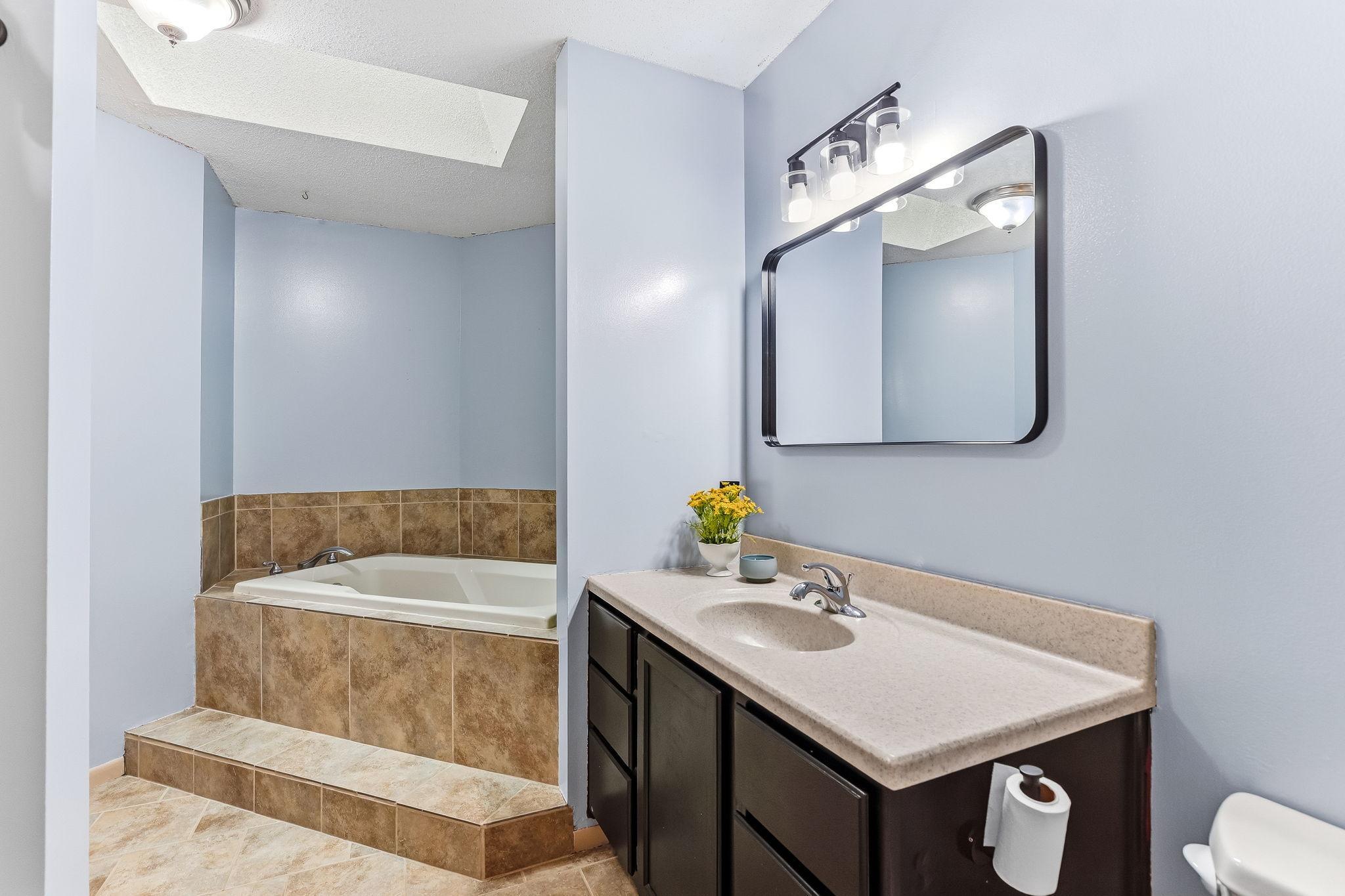Spacious full bathroom featuring oversized soaking tub, dark vanity, tile-style flooring, and generous counter space in this well-maintained Inver Grove Heights townhome near parks, shopping, and St. Paul.