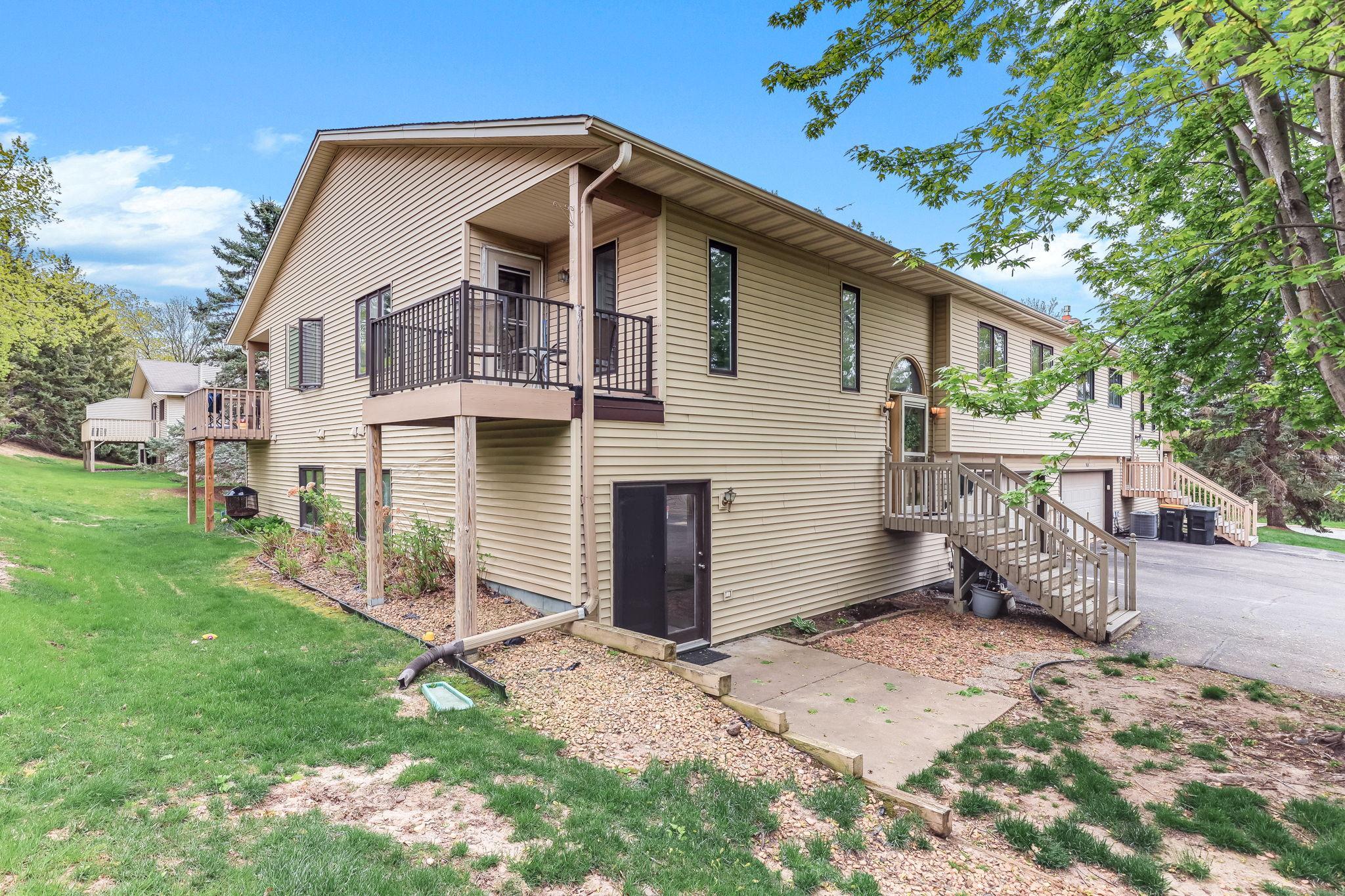 Rear exterior view showcasing the home’s multi-level layout, elevated deck space, walkout lower level, mature surroundings, and convenient outdoor access.