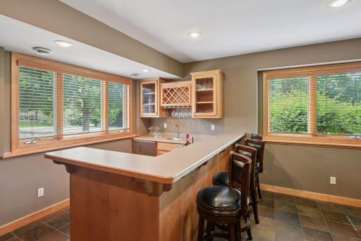 Beautifully designed wet bar showcases custom cabinetry, display shelving, stemware storage, and expansive countertop seating for guests. Egrees windows bring in a ton of natural light to this lower level space.