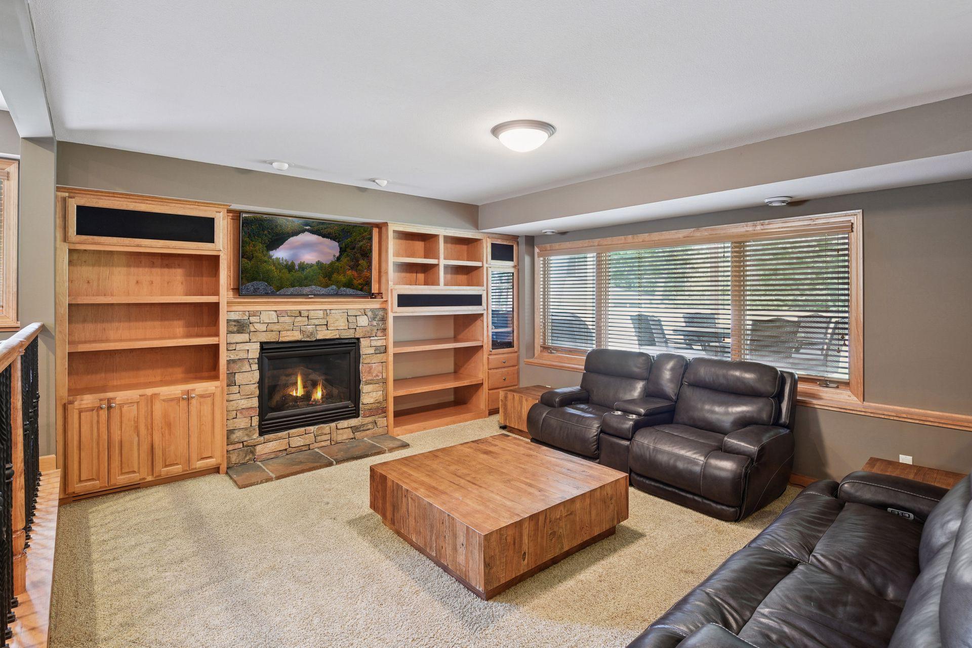 Comfortable lower-level family room centered around a stunning stone-surround gas fireplace with custom built-in shelving / cabinetry. Large lookout windows bring in abundant natural light while creating a cozy yet open gathering space.