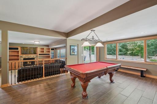 The spacious recreation area features a custom wet bar with extensive space, built-in wine storage, beverage refrigerator, and beautiful wood cabinetry accented by large windows and natural light.