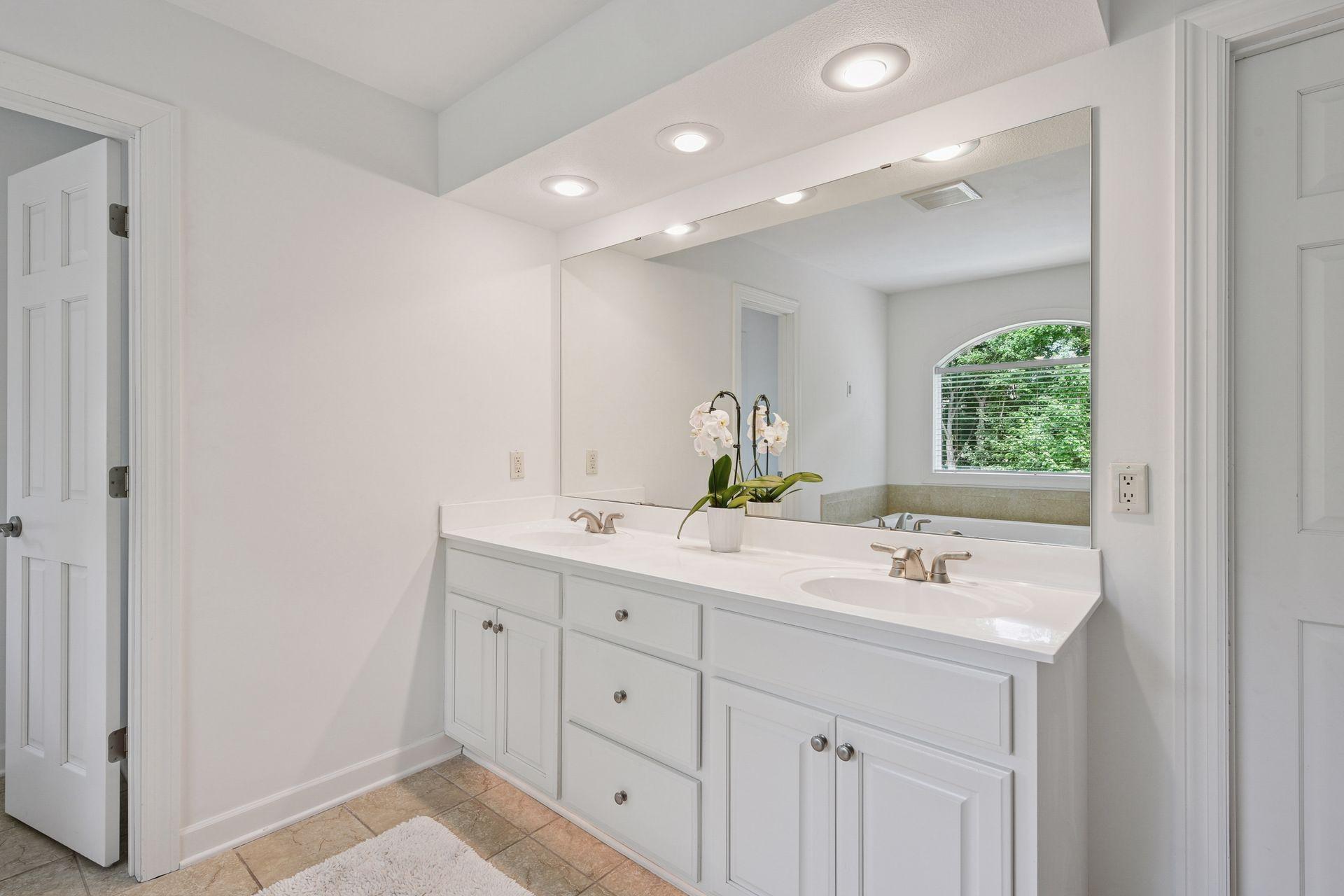 Thoughtfully designed primary bath showcases an expansive double vanity with generous counter space, updated lighting, and functional storage. Bright white finishes and oversized mirror create a clean, modern feel while maintaining timeless appeal.