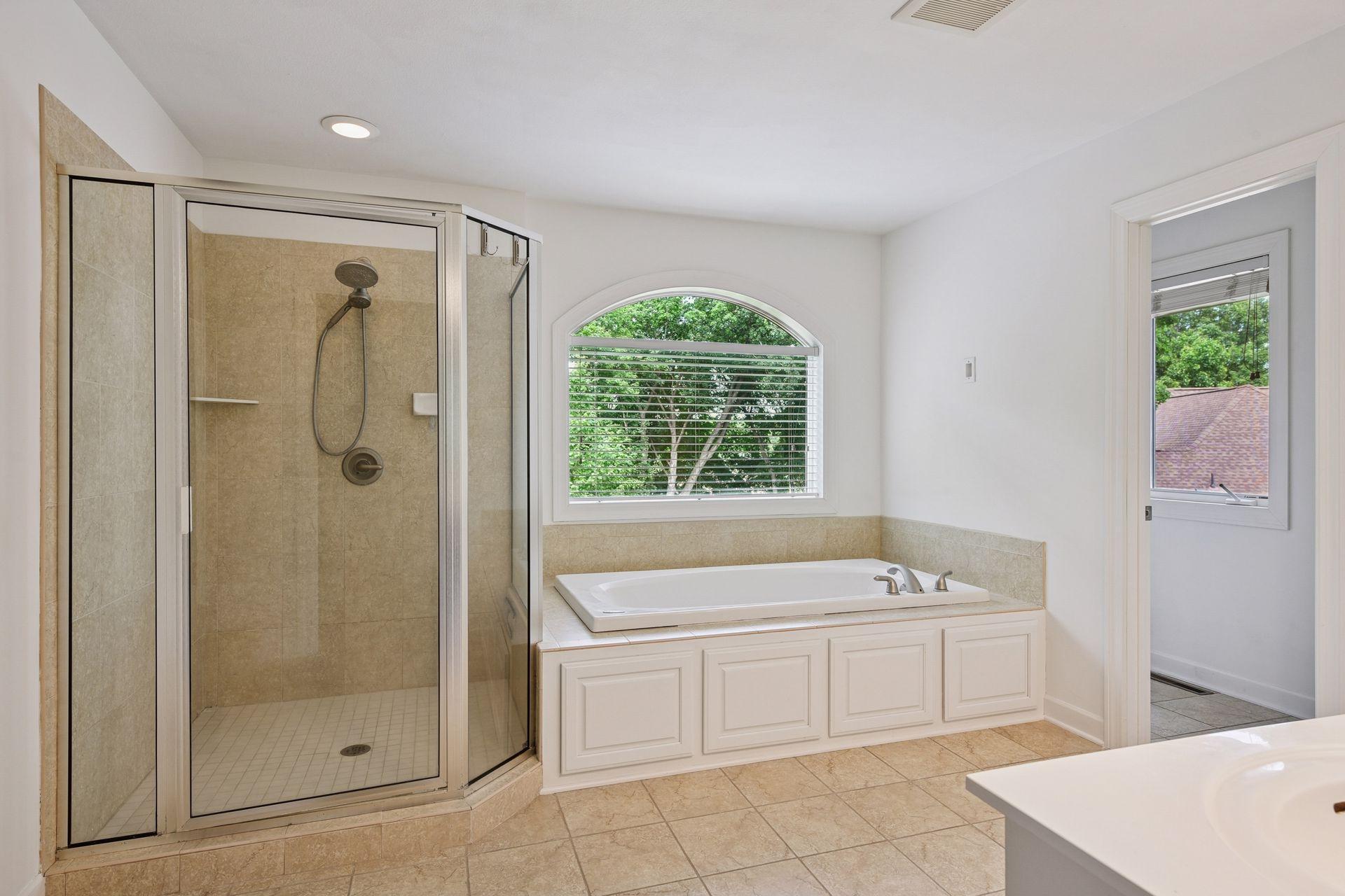 Spa-inspired primary bathroom features a soaking tub beneath an elegant arched window, separate walk-in shower, dual-sink vanity, and abundant natural light.