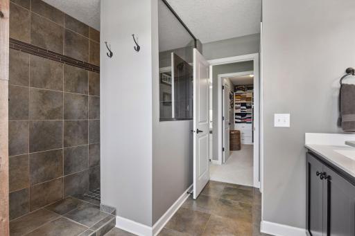 Custom tiled shower with dual shower heads. Through the doorway you can see a glimpse of the primary walk-in closet with custom organizers