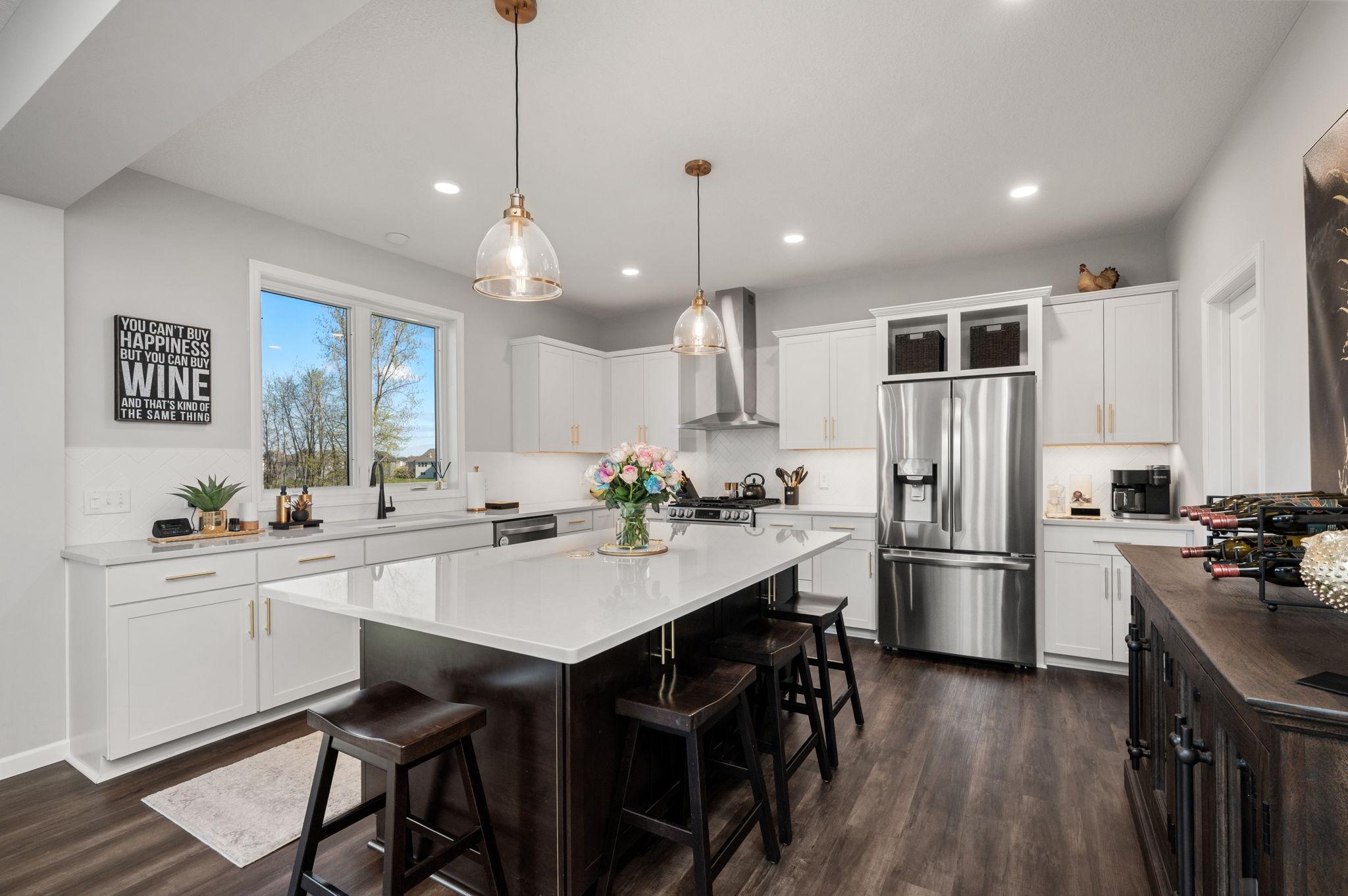 Gourmet kitchen designed for entertaining, complete with a massive center island, quartz countertops, herringbone tile backsplash, under-cabinet lighting, and high-end stainless steel appliances with a range hood