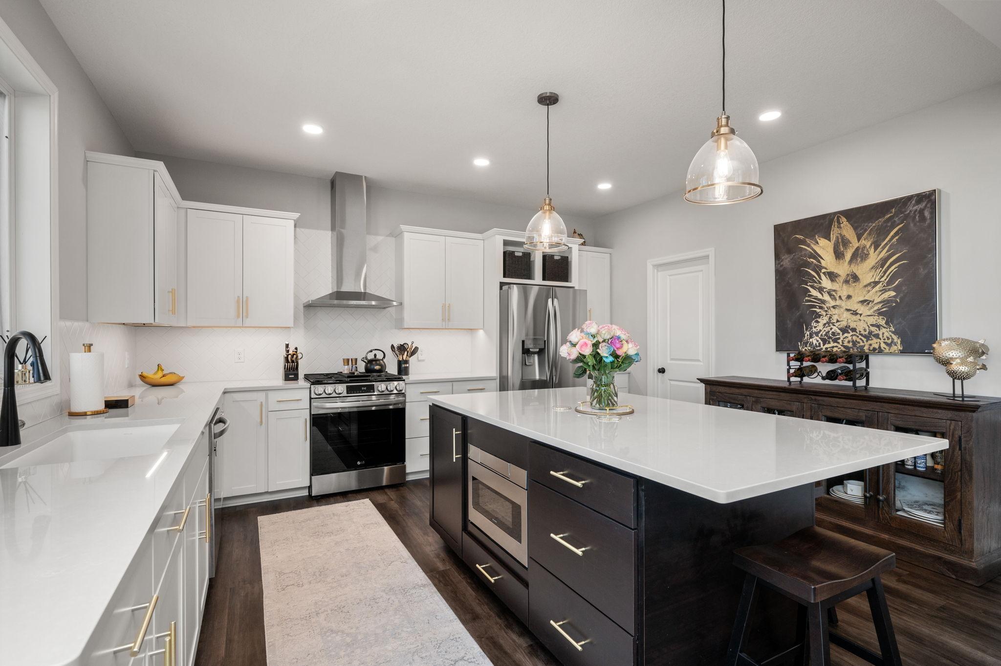 Gourmet kitchen designed for entertaining, complete with a massive center island, quartz countertops, herringbone tile backsplash, under-cabinet lighting, and high-end stainless steel appliances with a range hood