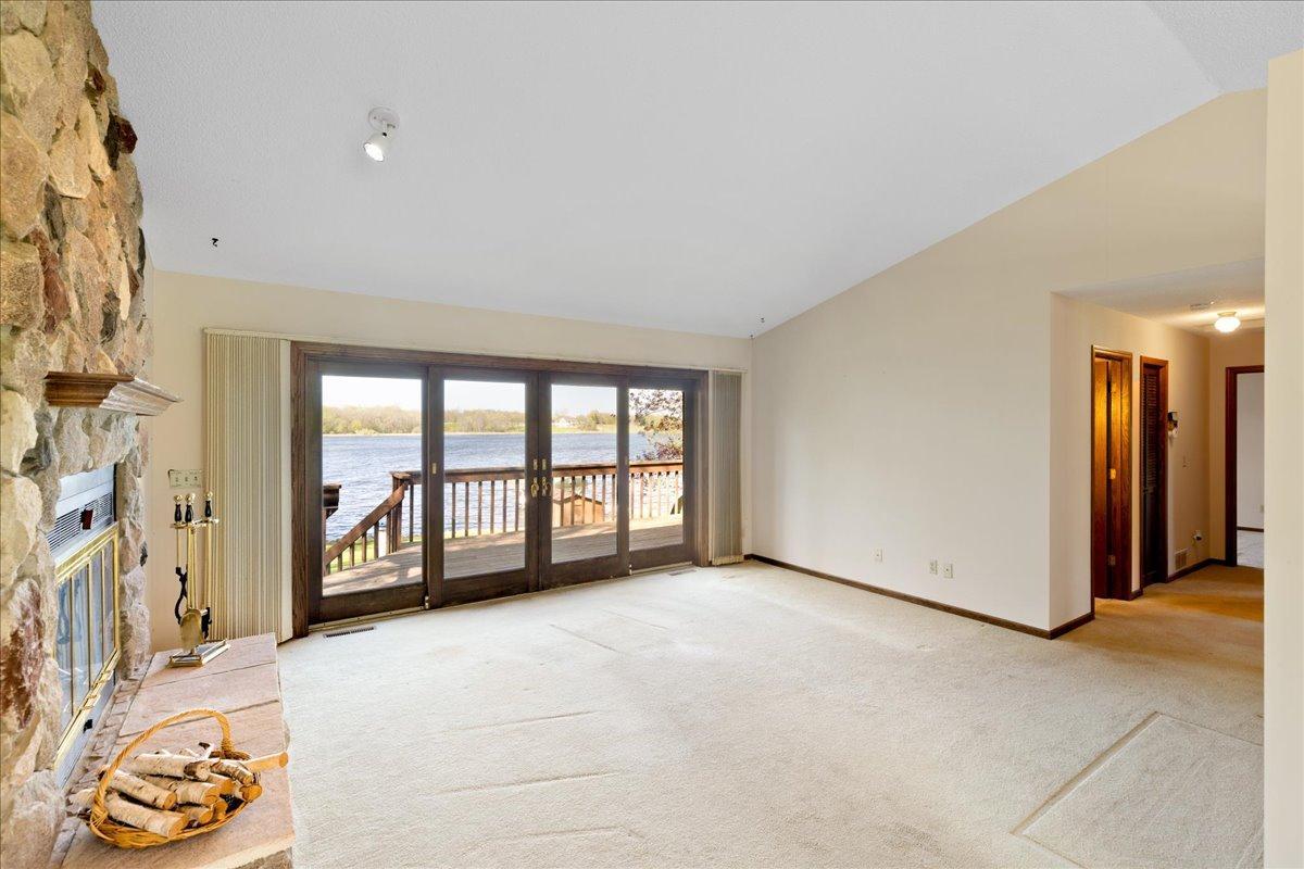 Large living room featuring vaulted ceilings, a stone fireplace, and expansive lakeside windows.