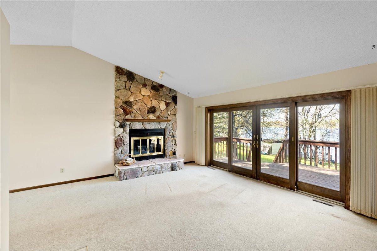 Large living room featuring vaulted ceilings, a stone fireplace, and expansive lakeside windows.
