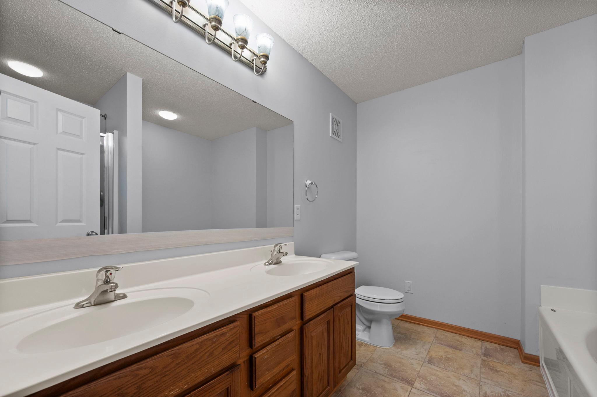 The private primary bathroom features a large vanity with double sinks, oak cabinetry, and a large mirror.