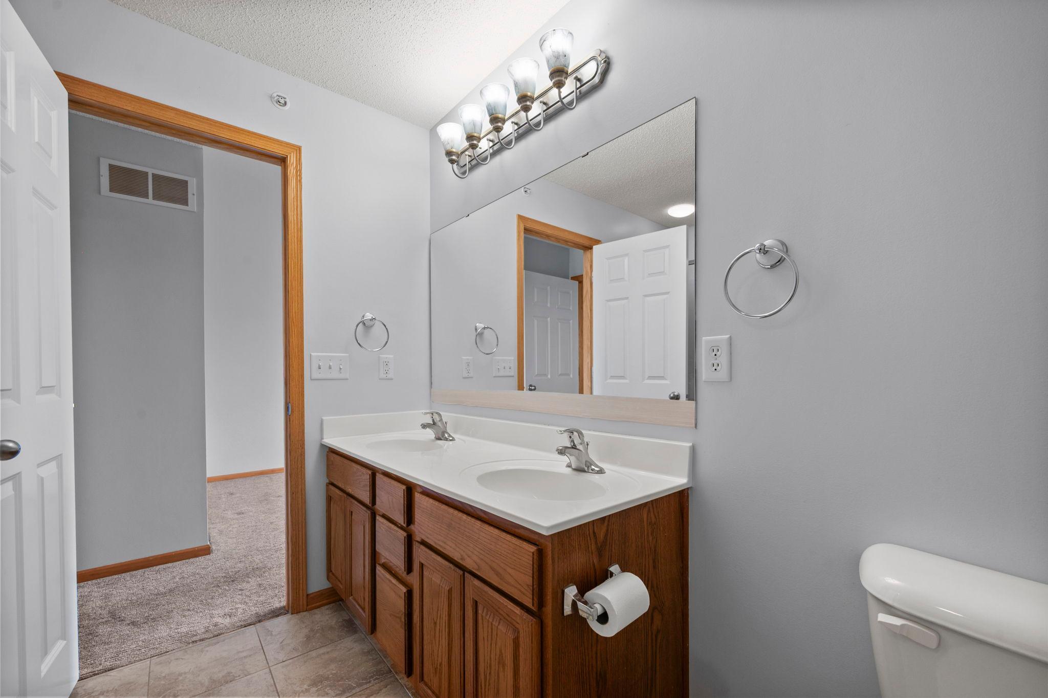 Another view of the primary bath showing the double vanity, updated lighting, and durable tile flooring.