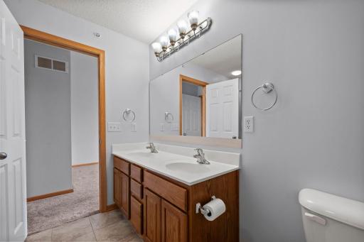 Another view of the primary bath showing the double vanity, updated lighting, and durable tile flooring.