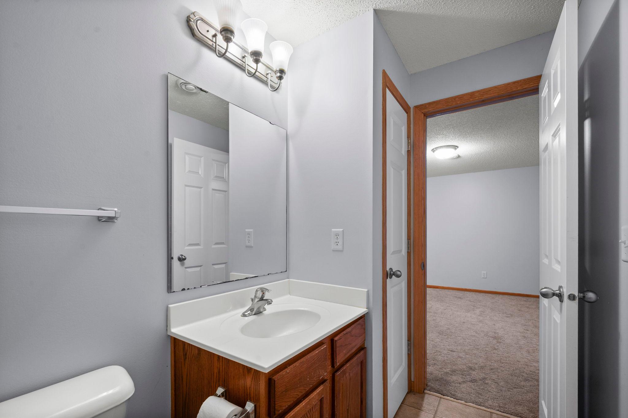 The lower-level bathroom is complete with a wood vanity, large mirror, and bright lighting.