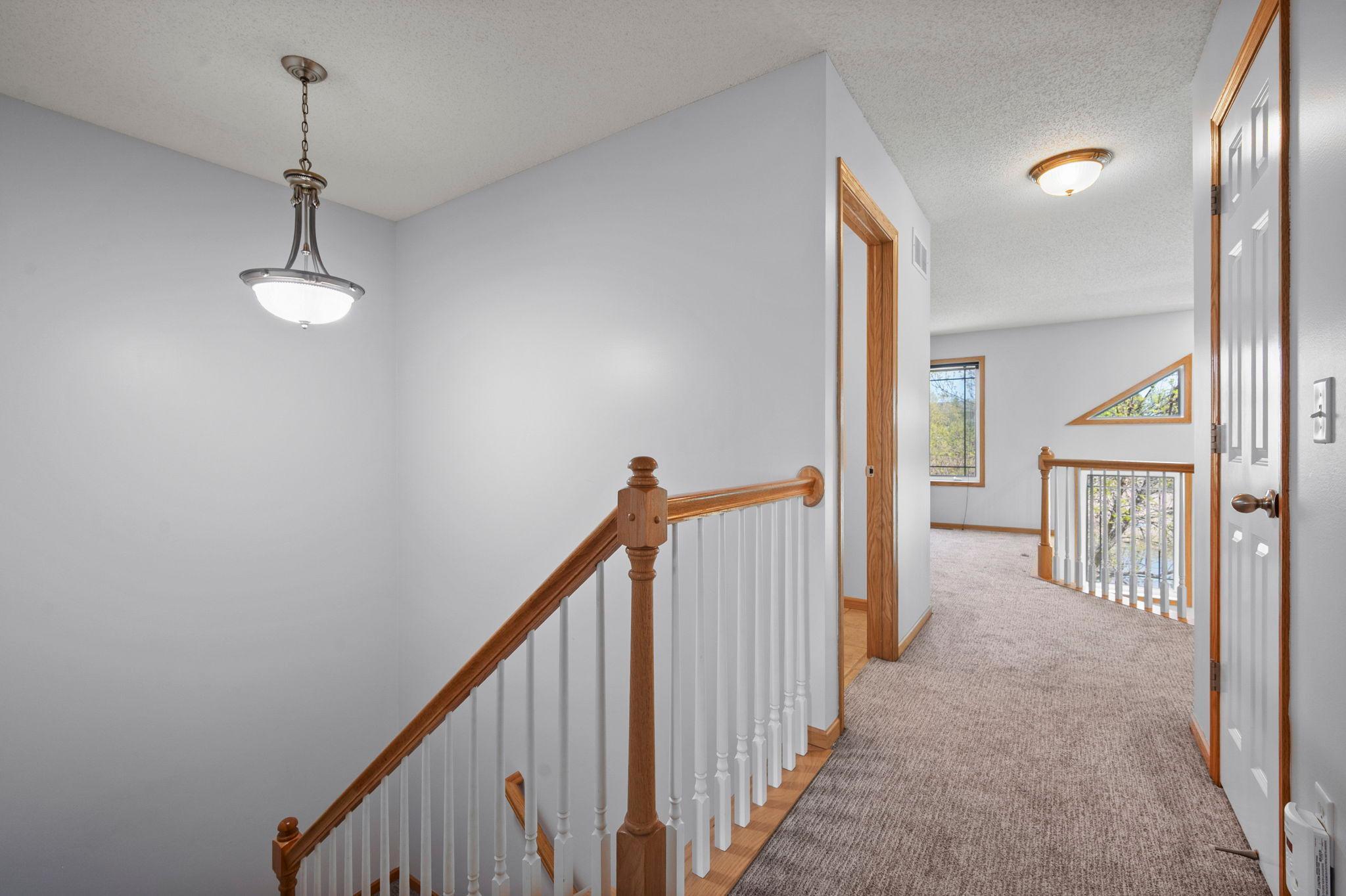 The upper-level landing features an elegant staircase with wood railings and overlooks the lower level.