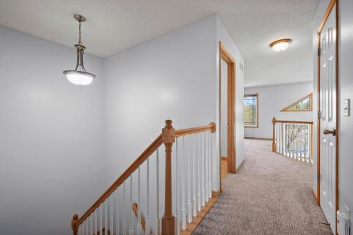 The upper-level landing features an elegant staircase with wood railings and overlooks the lower level.