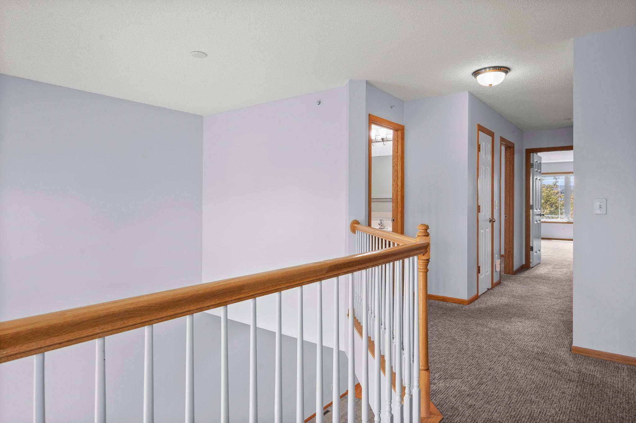 The upper hallway is well-lit and features classic wood railings that complement the home's neutral interior.