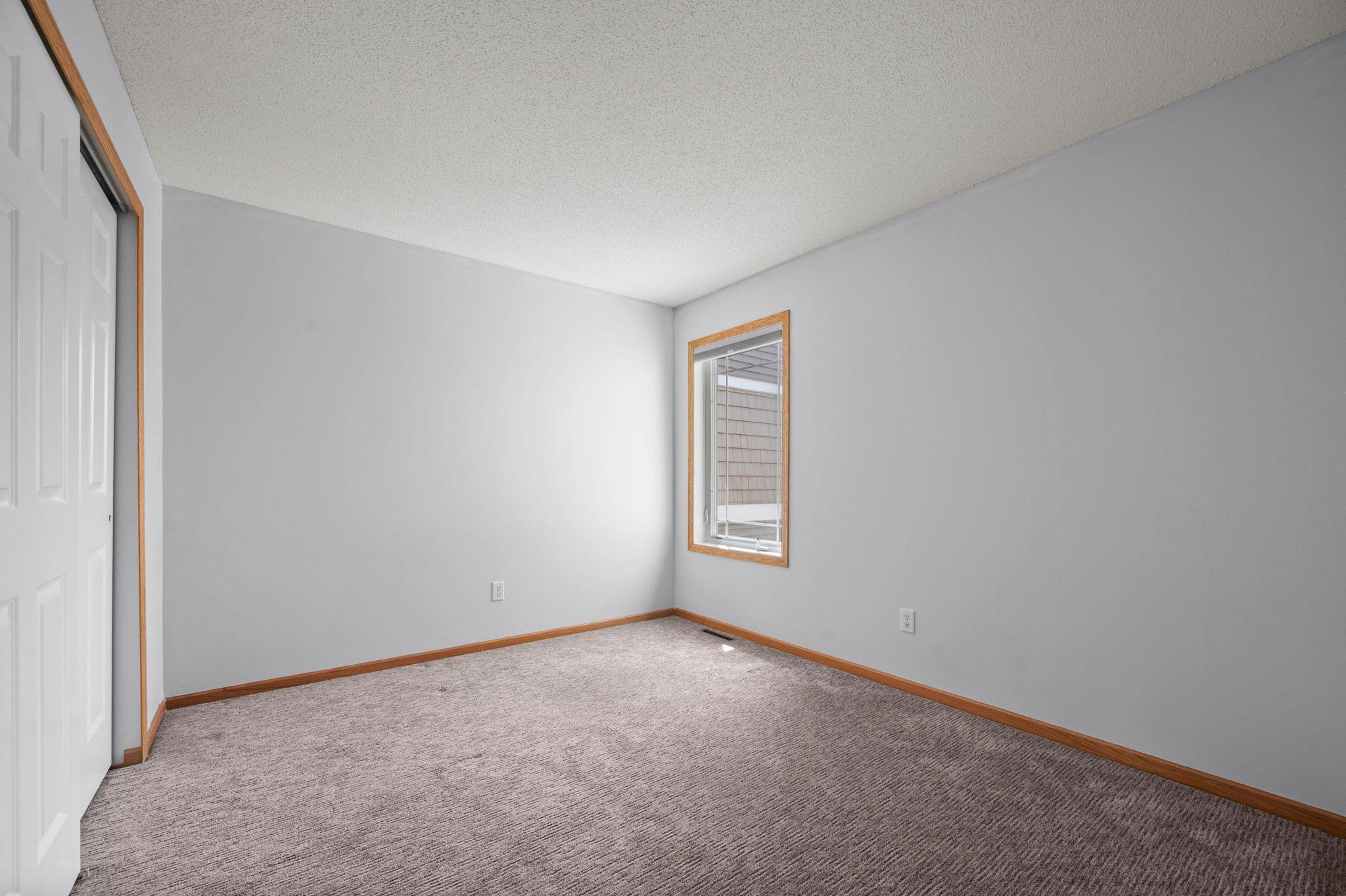 This secondary bedroom includes a large window and a spacious closet with sliding white doors.