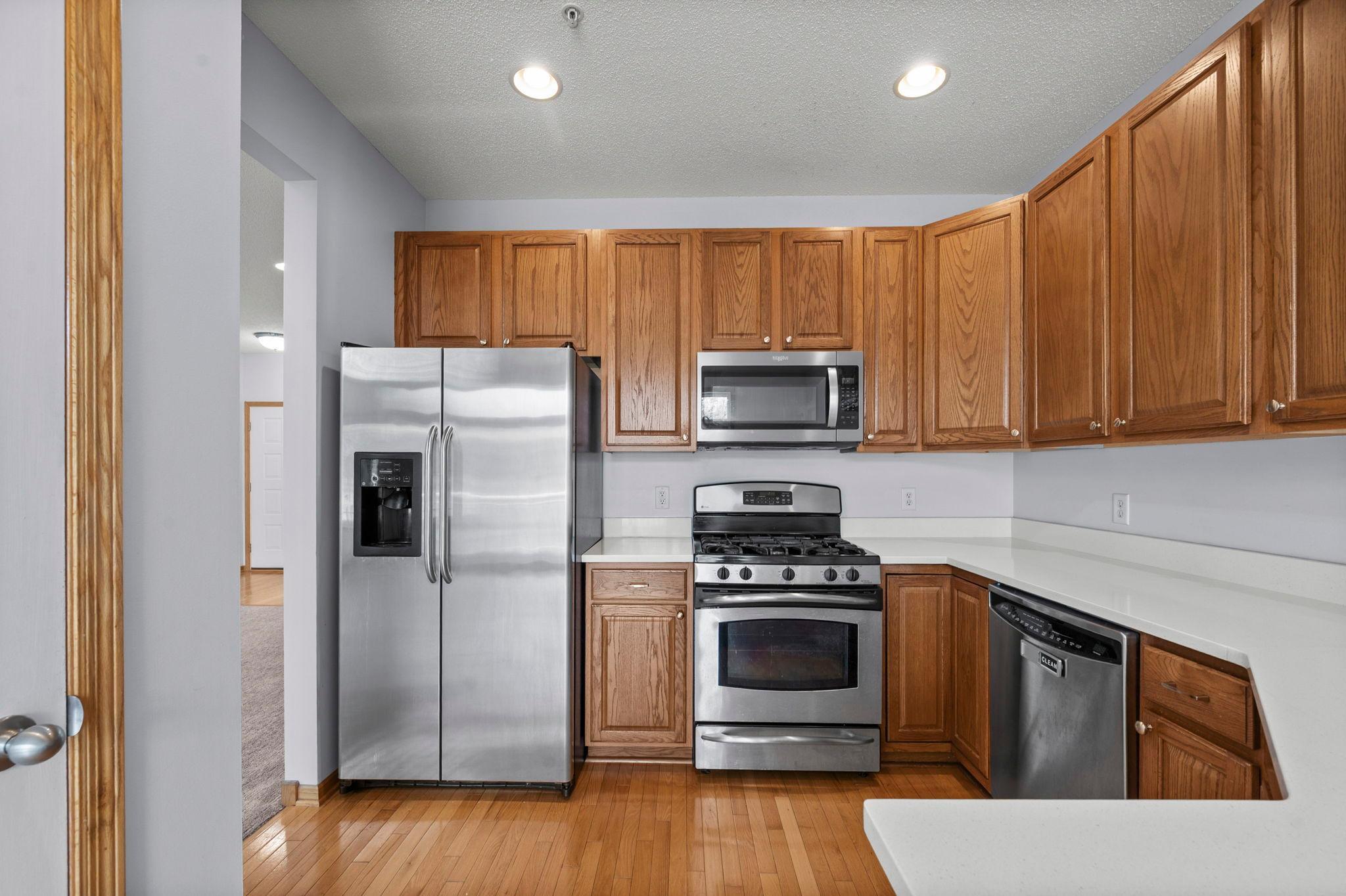 This perspective highlights the modern stainless steel refrigerator and gas range, perfectly integrated with the classic wood cabinets.