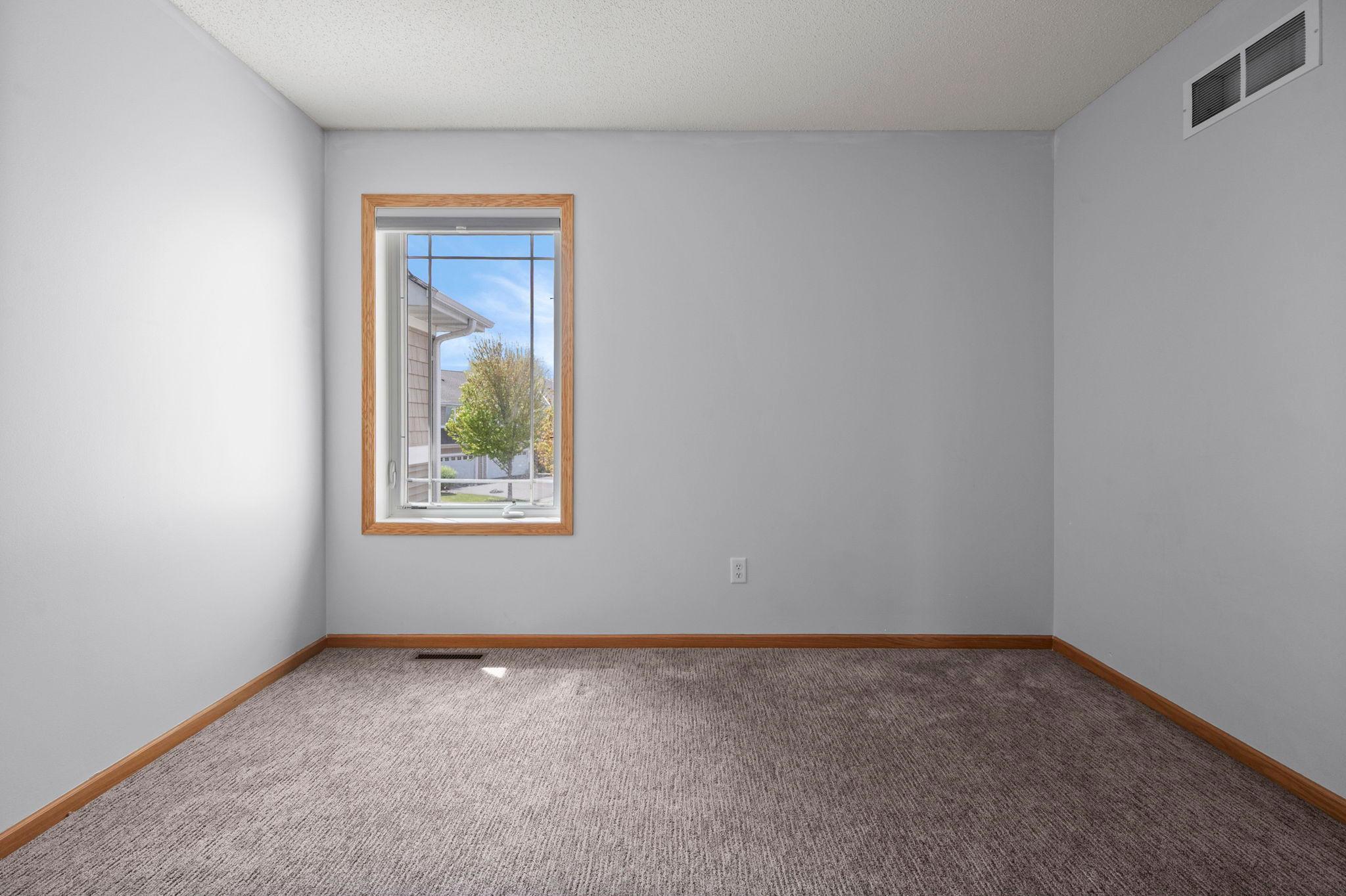 A bright and clean secondary bedroom, perfect for guests or family, featuring neutral paint and plush carpeting.