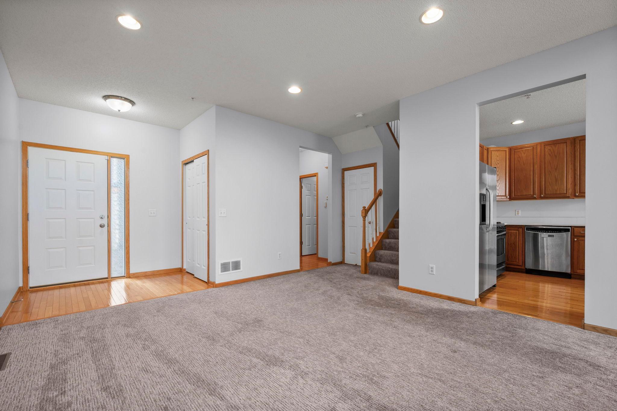 Inviting foyer with beautiful hardwood flooring, a convenient coat closet, and neutral carpeting.
Open-concept entryway showing the seamless flow from the front door into the main living areas and kitchen.