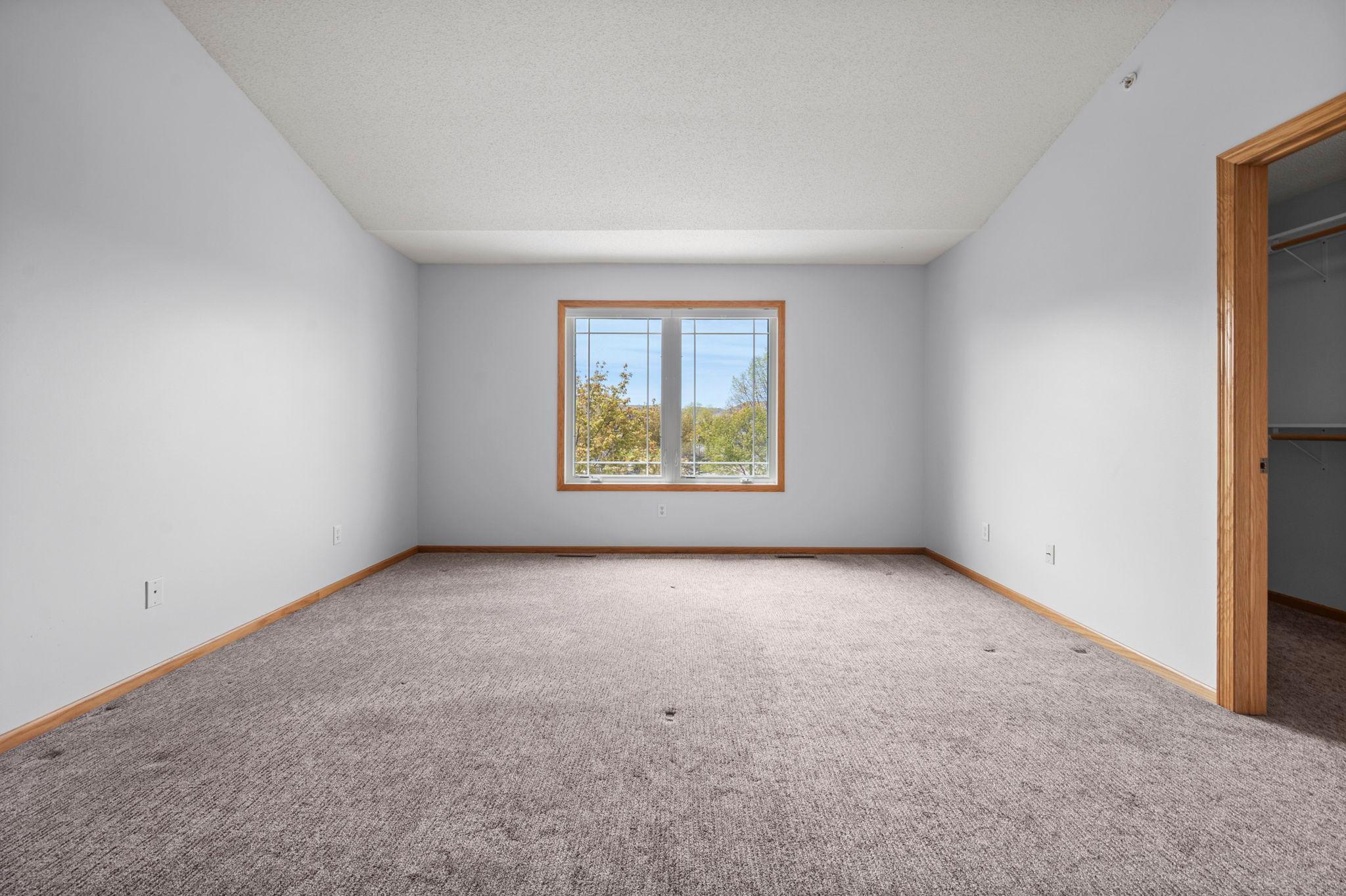 The spacious primary bedroom offers vaulted ceilings, neutral carpeting, and a large window overlooking the grounds.