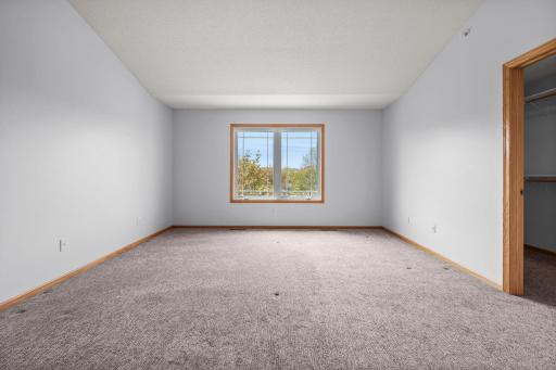 The spacious primary bedroom offers vaulted ceilings, neutral carpeting, and a large window overlooking the grounds.