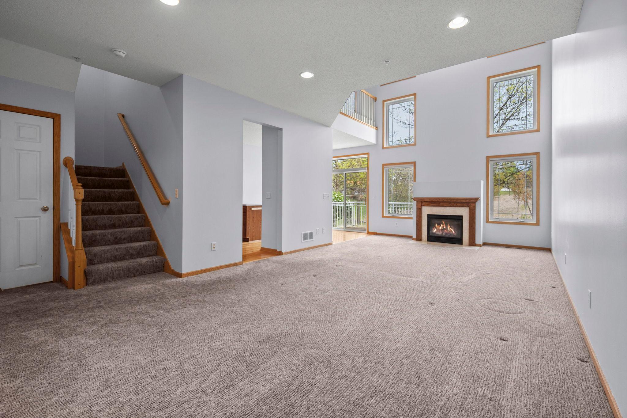 Dramatic living room featuring soaring two-story ceilings and a cozy gas fireplace with a wood mantel.
