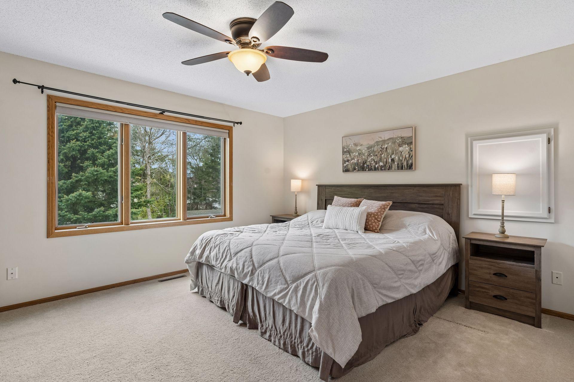 Spacious upper level primary bedroom with large window and ceiling fan.