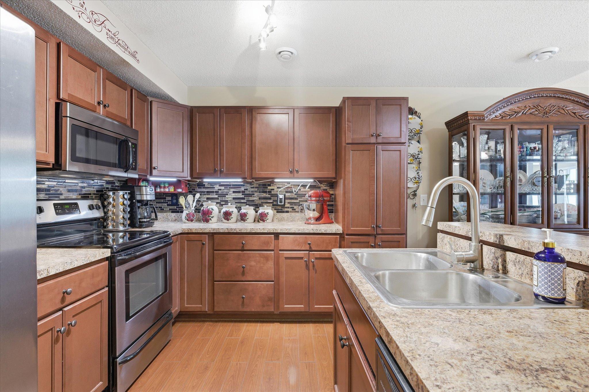 Beautiful kitchen featuring rich cherry cabinetry, stainless steel appliances, a large pantry, stylish tile backsplash, and abundant counter space.