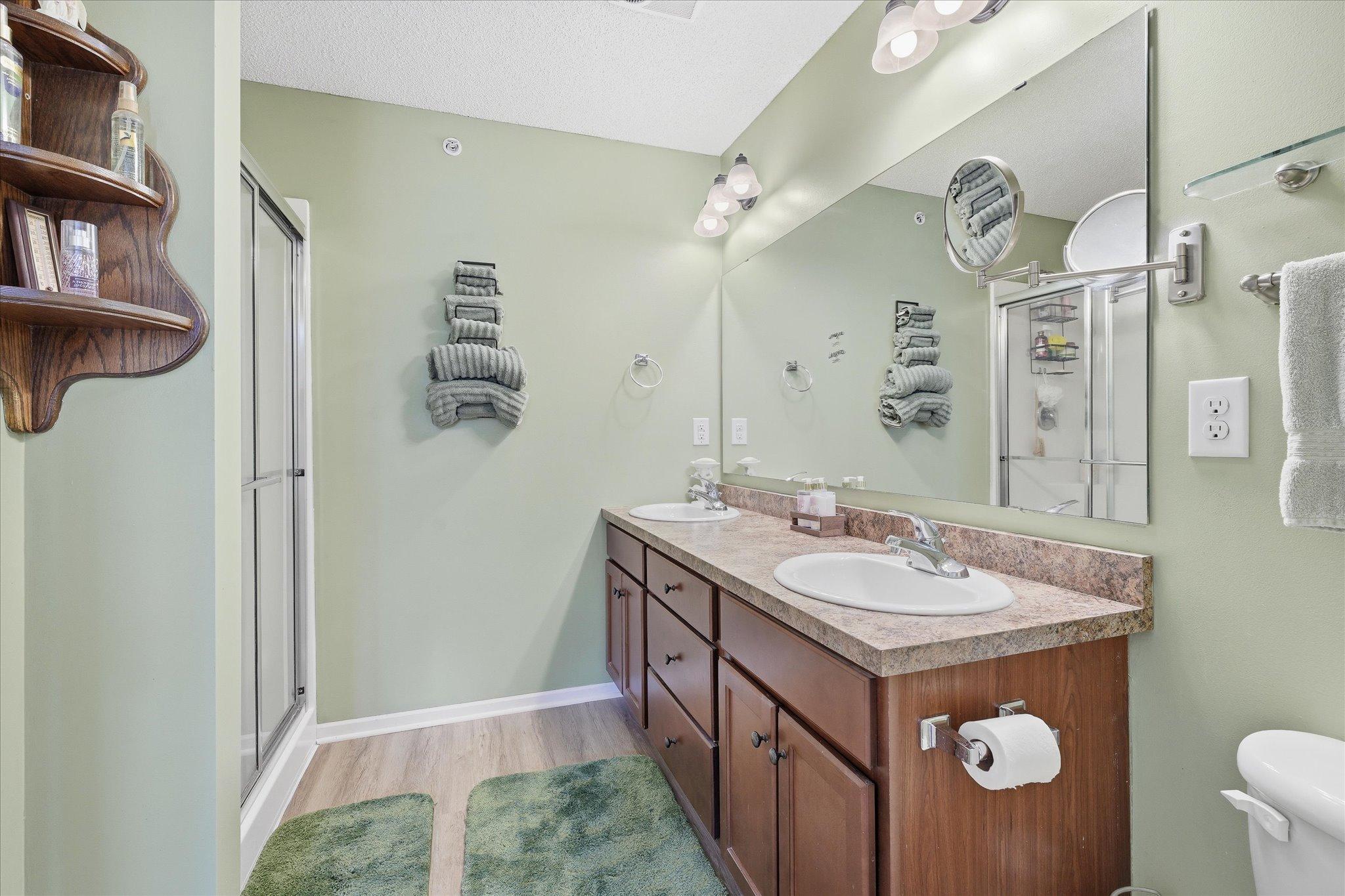 Private primary bathroom offering dual sinks, extended vanity space, linen closet, and walk-in shower with glass doors.