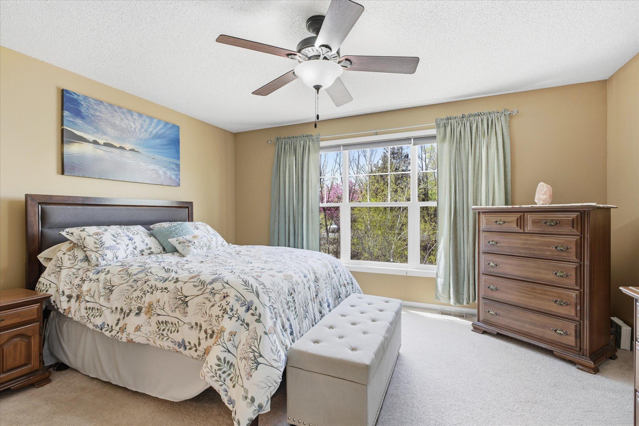 Spacious primary suite filled with natural light and peaceful views overlooking mature trees.