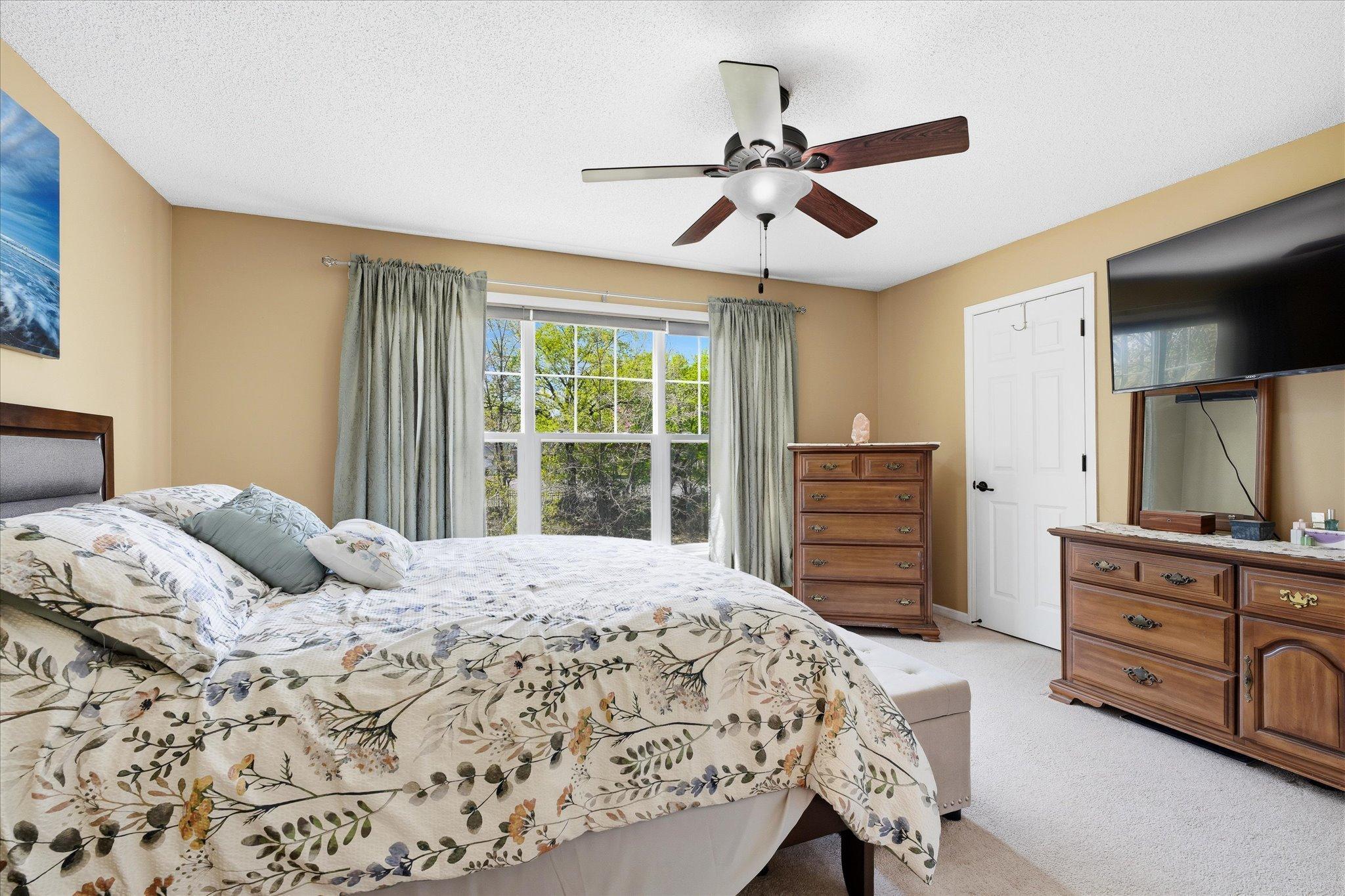 Large primary bedroom with neutral finishes, ceiling fan, and plenty of space for additional furniture or seating area.