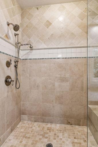 The curb-less tiled shower features a frameless glass enclosure and a built-in bench.