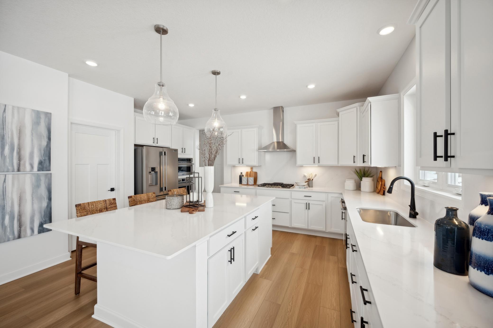 (Photo of a decorated model, actual homes finishes will vary) The spacious gourmet kitchen features a large center island, quartz countertops, LVP floors, stainless appliances and more!