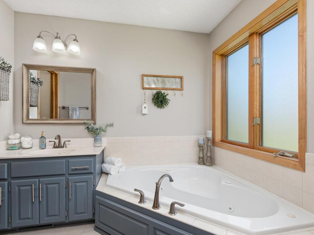 Chic primary bathroom suite: Separate jetted tub, walk-in shower, bright natural lighting, newer light fixture, toilet, faucet/hardware and showerhead and a modern, stylish color palette.