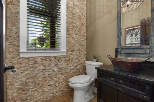 Striking floor to ceiling natural stone creates a dramatic backdrop in this designer powder room, complete with a custom vessel sink and rich wood vanity.