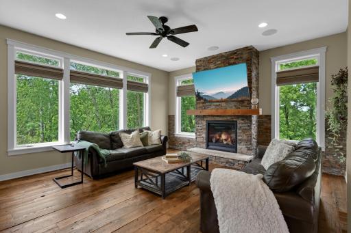 Walls of windows bring the outdoors in, while the floor-to ceiling stone fireplace creates a dramatic focal point in this spacious living room.