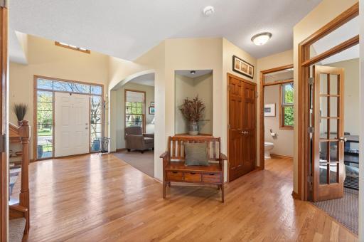Step inside to a welcoming foyer with hardwood floors and large windows flooding the space with natural light, giving the home a bright and airy feel. Notice the dual staircase and charming built-in niches, benches, and shelves found throughout.