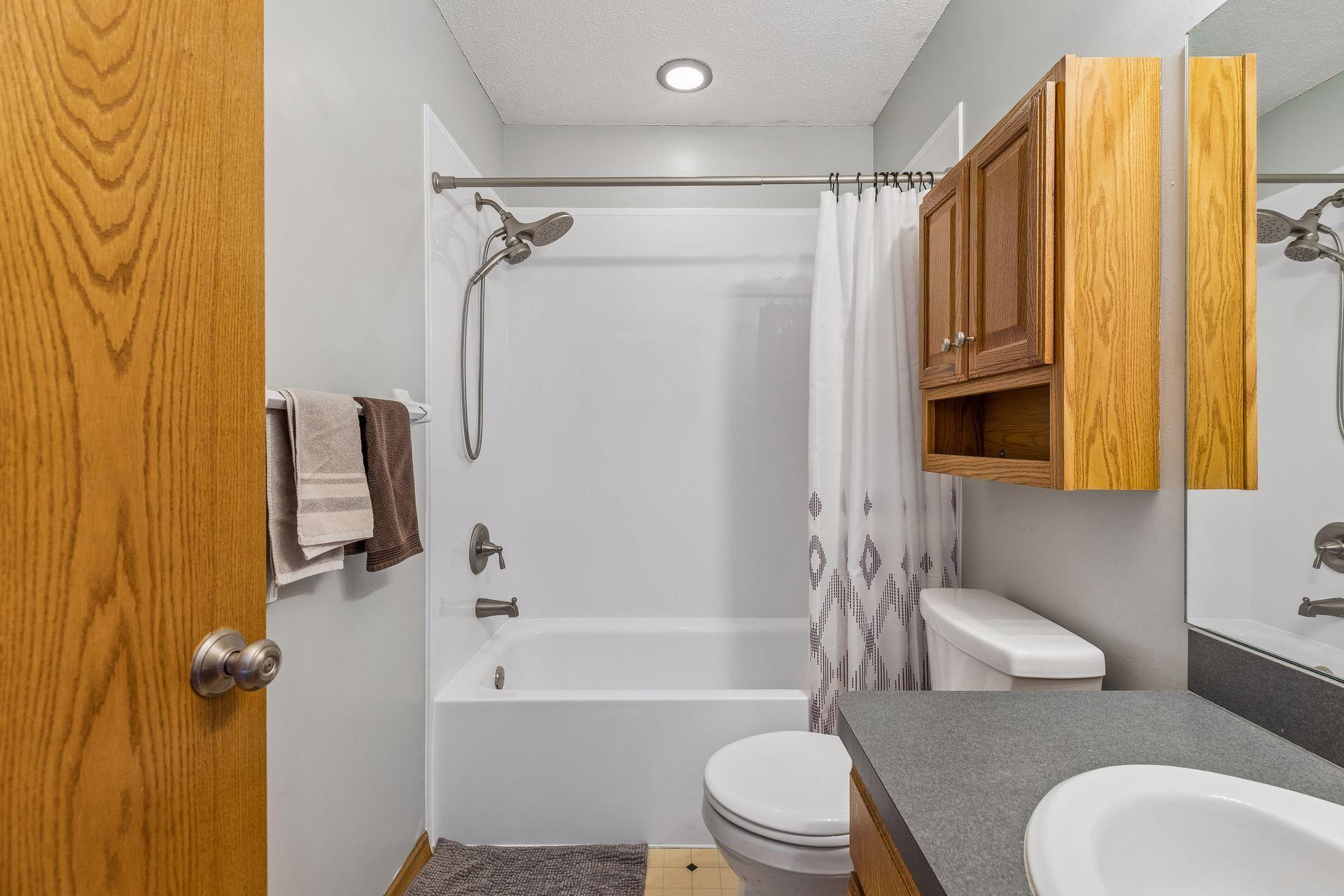 Enjoy this refreshed upper level full bath with a 2025 tub/shower insert, new (2025) toilet, vanity sink, storage cabinet, linoleum floors, and overhead lighting for convenience.
