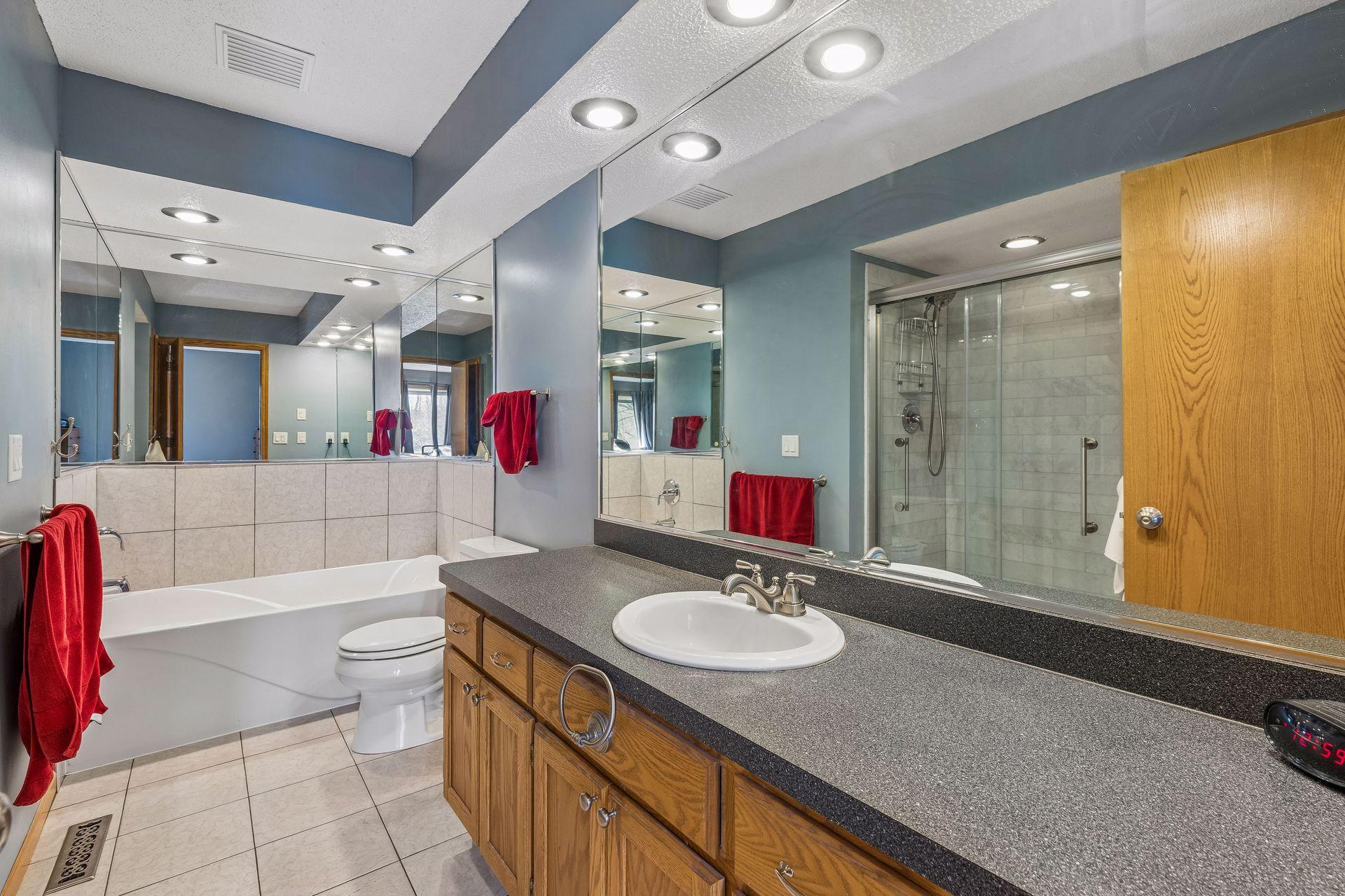 Relax in the spacious primary bath with a large vanity sink, separate tub and shower, tile floors, and bright overhead lighting.